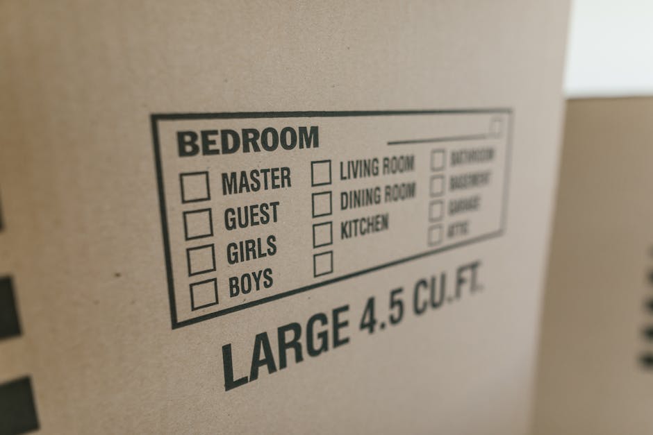 A close-up view of a cardboard box with printed labels indicating various room categories such as 'Bedroom', with options for 'Master', 'Guest', 'Girls', and 'Boys', each accompanied by empty checkbox
